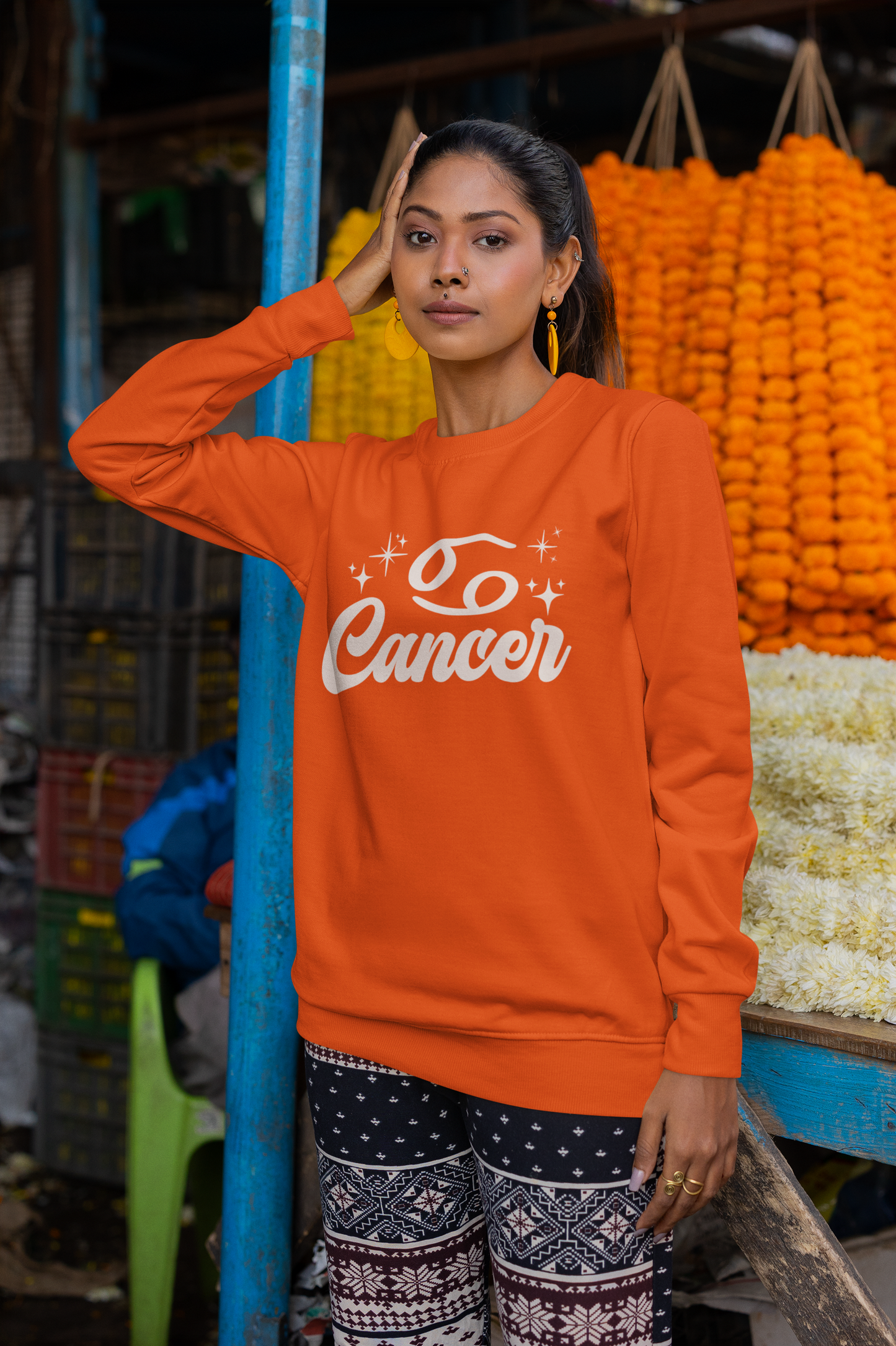 Woman wearing a orange sweatshirt with 'Cancer' white text in an outdoor market setting