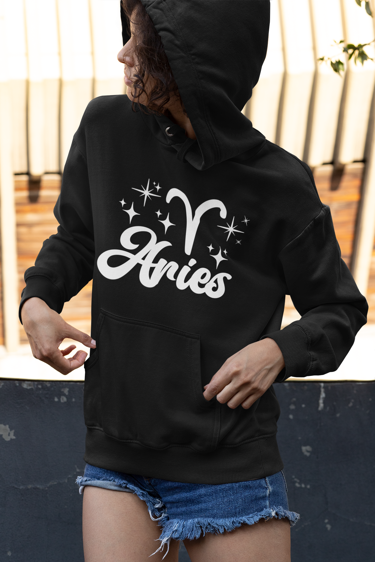 Person wearing a black hoodie with 'Aries with zodiac symbol' white text, standing outdoors.