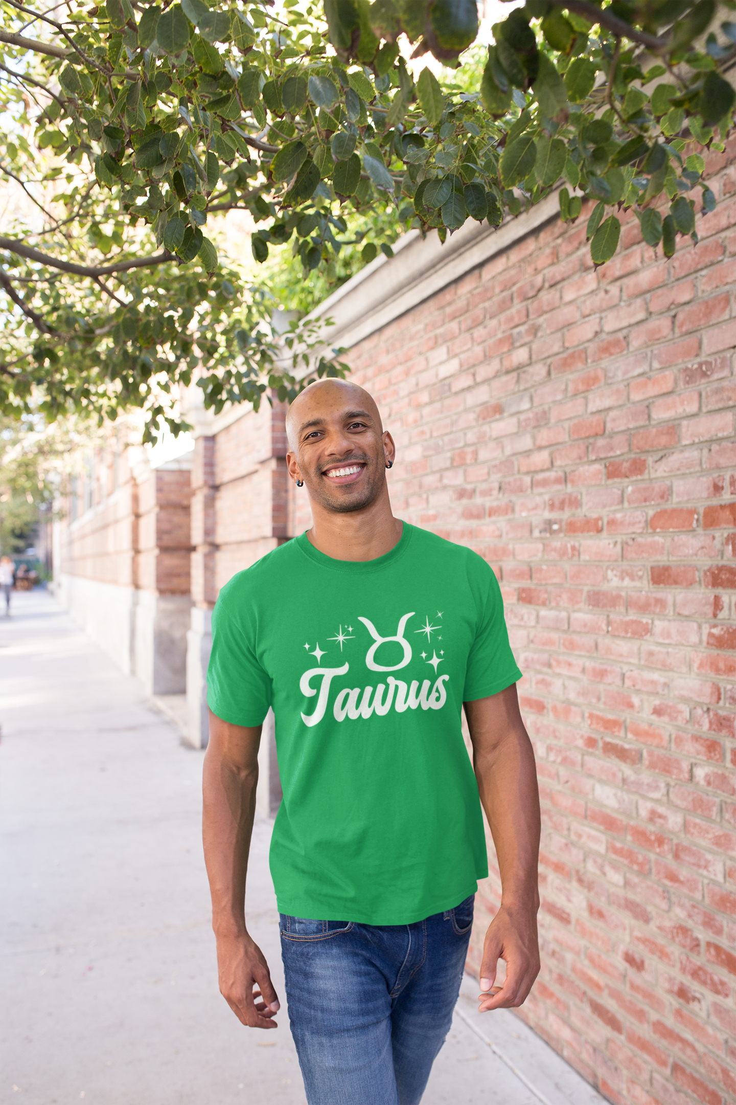Man wearing a green t-shirt with 'Taurus' white text design, walking outdoors near a brick wall and tree.