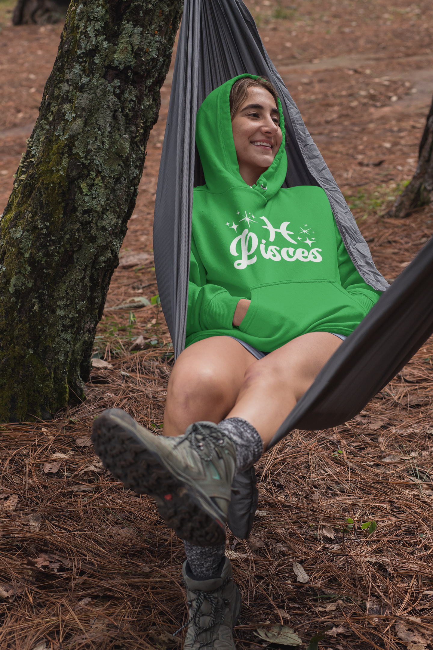 Person sitting in a hammock outdoors wearing a green hoodie with 'Pisces' white text with zodiac symbol.