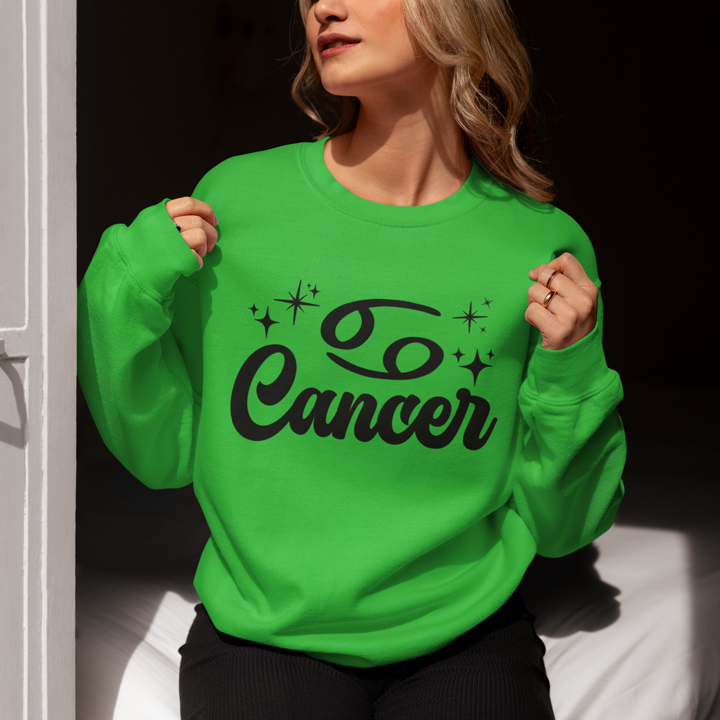 Person wearing a green sweatshirt with 'Cancer' black text, sitting indoors.