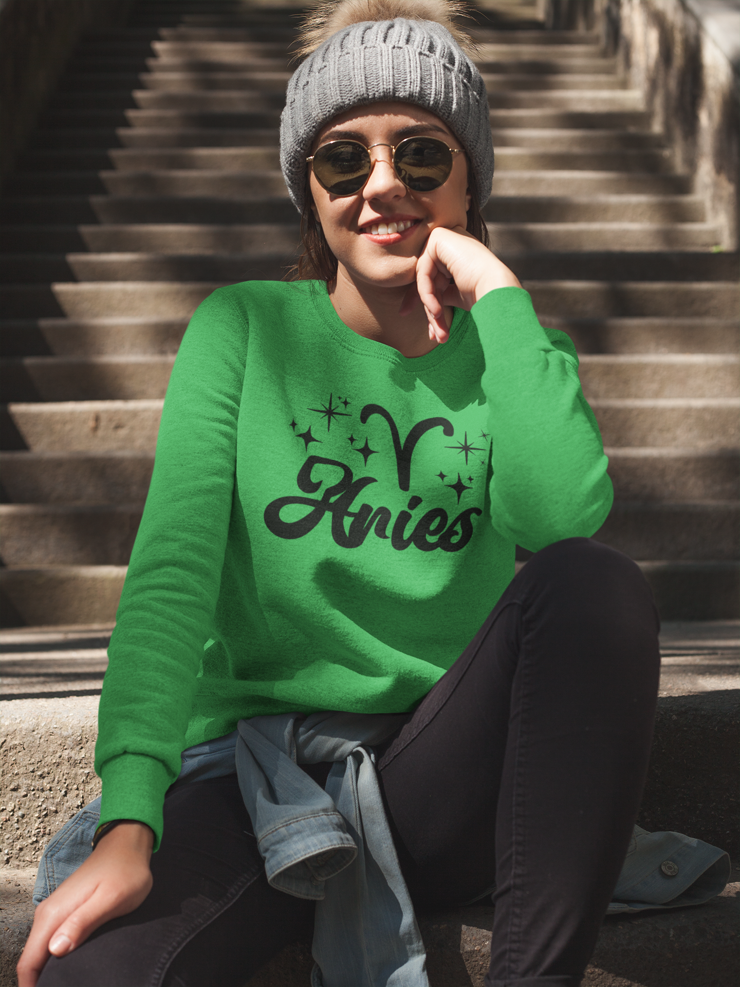 Person wearing a green 'Aries' black text design sweatshirt sitting on steps.