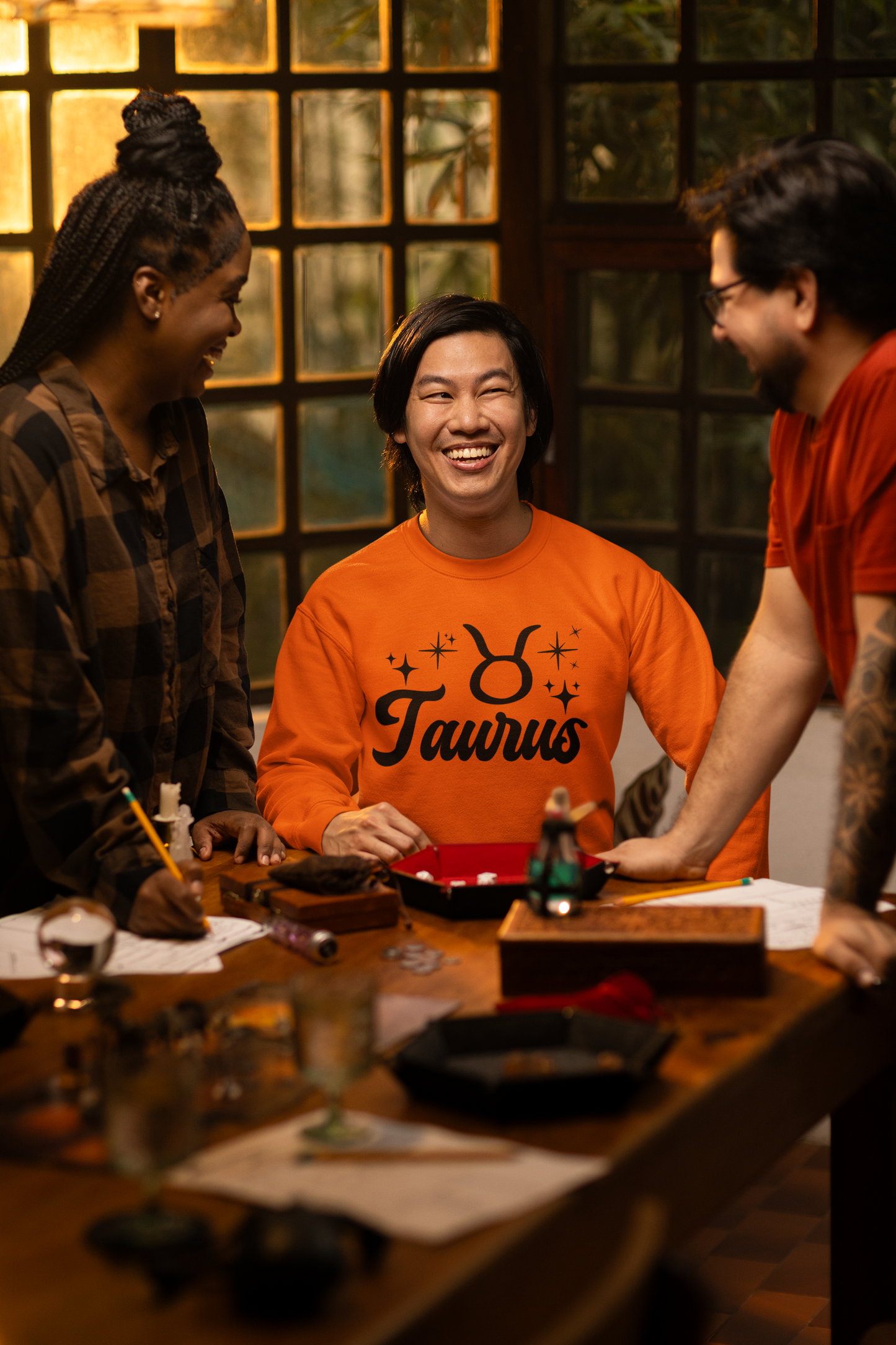 Three people around a table with a focus on a person wearing a orange 'Taurus' black text t-shirt.