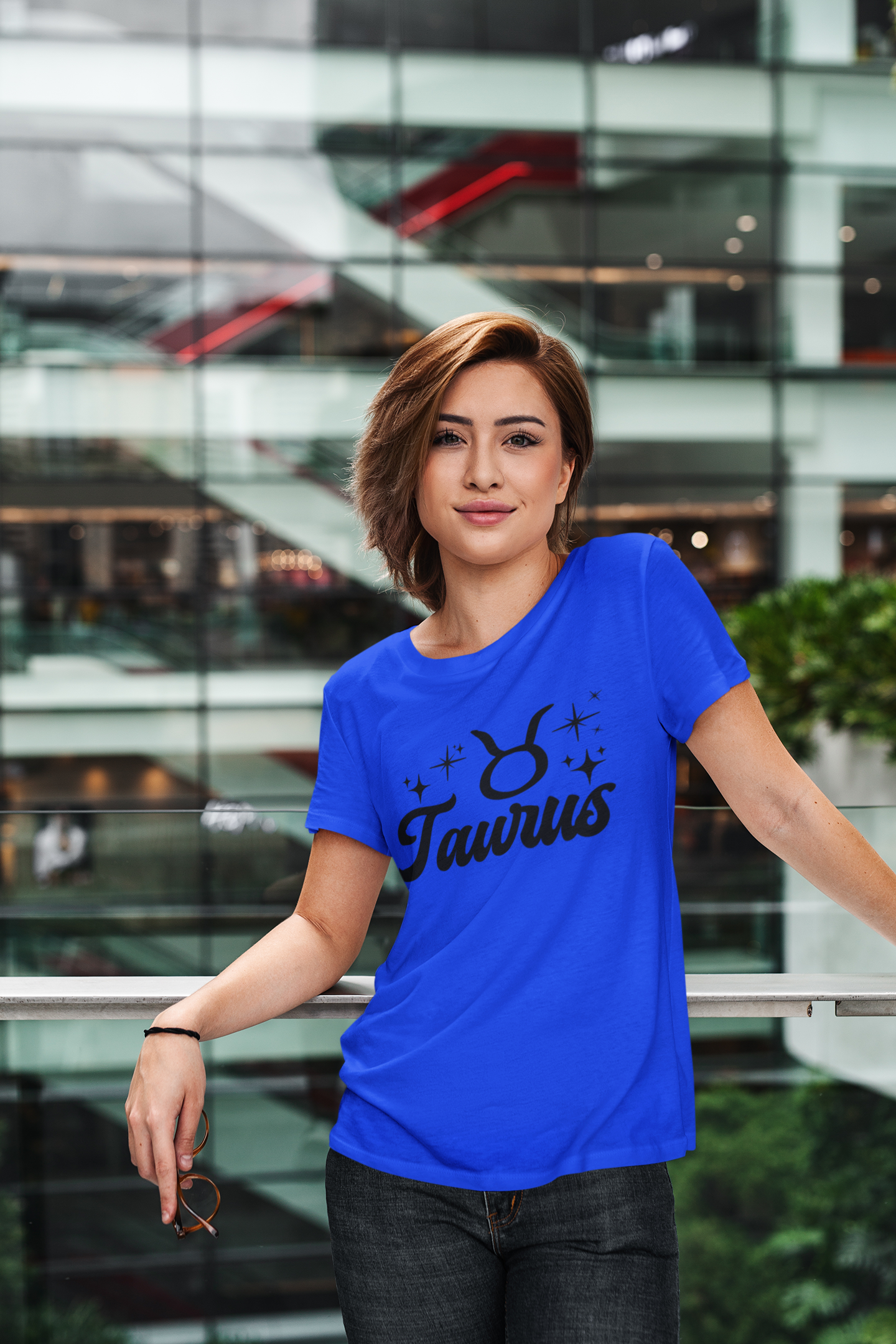 Person wearing a blue Taurus t-shirt, black text design in front of a modern building.
