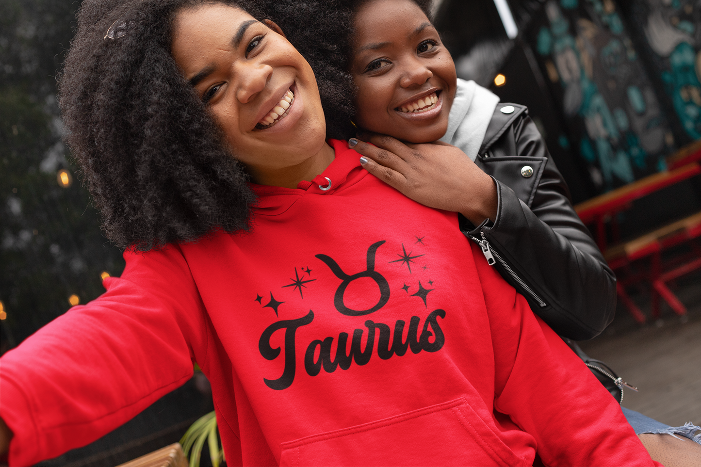 Two people posing together, one wearing a red 'Taurus' hoodie, black text design 