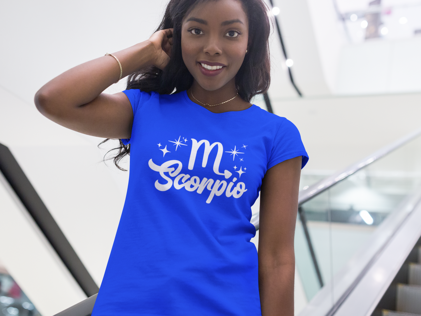 Woman wearing a blue t-shirt with 'Scorpio' white text design, standing on escalator.